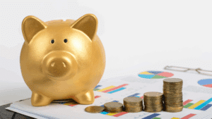 A golden piggy bank sits on a table covered in colorful graphs, next to stacks of coins